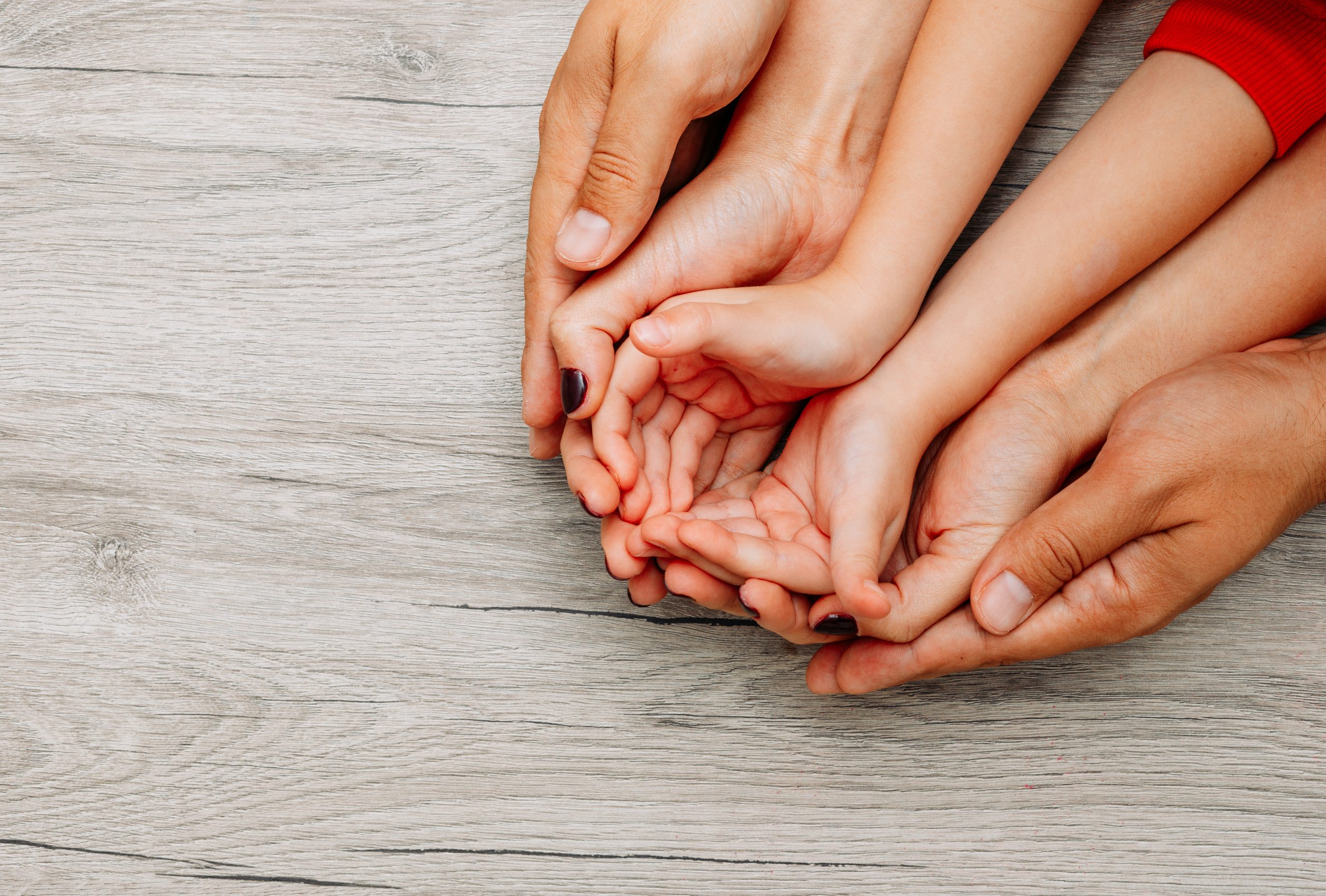 father, mother and daughter holding hands on top of each other on a light wooden background. top view.